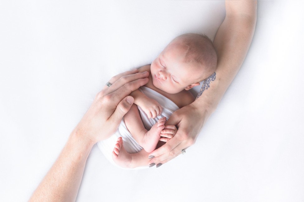 newborn baby with parents hands around her