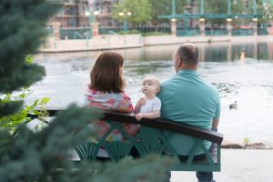 baby photographer shows baby with parents at lake